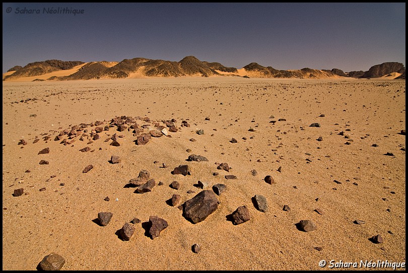 alidemma-4.jpg - La nécropole de Monkhor. Les petits amas de pierres indiquent les lieux de sépultures de bovins. Si ces sépultures sont fréquentes dans l'Egypte ancienne, elles sont quasi inconnues dans le Sahara. On dénombre une trentaine de tombes sur le site. On peut penser que ce lieu a fonctionné comme un espace de cérémonie lié aux pratiques d'une population d'éleveurs.
