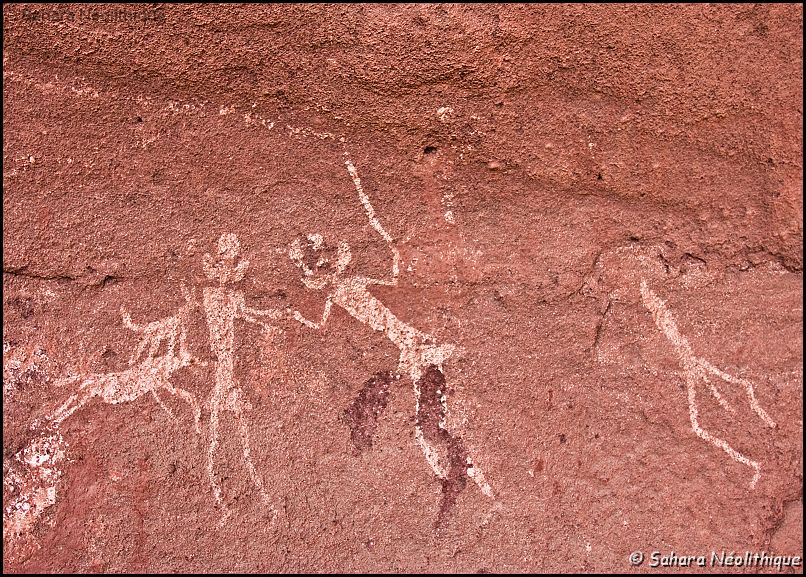 40d-IMG_4208a.jpg - Ouan Adjane. Personnages en aplat blanc avec des têtes trilobées. Celui du centre tient un baton et semble menacer le personnage de gauche. Celui de droite est remarquable par l'appendice qui pend entre ses jambes. Largeur du tableau: environ 0,45 m. 
Ces peintures sont a mettre au compte de l'école du "guerrier libyen".