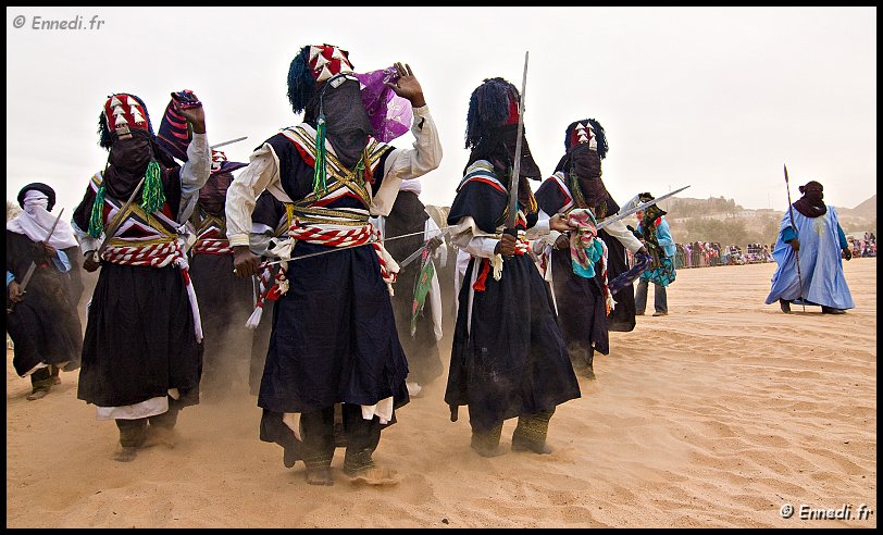 sebeiba-10.jpg - Le chef, l'amghar (l'homme avec la tunique bleu), est le maître de cérémonie. Chaque camp a un amghar qui veille à la performance de son équipe. Il vérifie les tenues, orchestre les mouvements de chacun, lance des injonctions, exhorte à mieux danser. Son rôle est déterminant pour l'émulation du groupe.